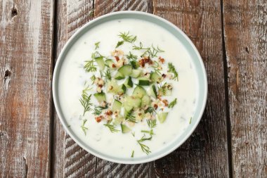 Ahşap masada dereotlu ve fındıklı lezzetli salatalık çorbası.