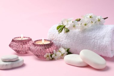 Kaplıca kompozisyonu yanan mumlar, çakıl taşları ve dallarla pembe arka planda güzel çiçekler, yakın plan