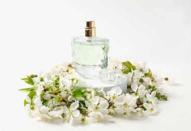 Podyumda bir şişe aromatik parfüm ve beyaz arka planda güzel çiçekli dallar, yakın plan. Ürünün şık sunumu