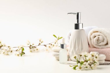 Spa ürünleri, çakıl taşları ve beyaz masadaki güzel çiçekli dallar, yakın plan.