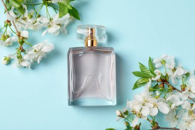 Bir şişe aromatik parfüm ve açık mavi arka planda güzel çiçekli dallar.
