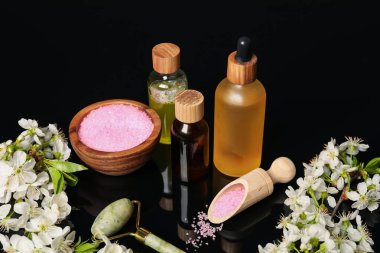 Siyah ayna yüzeyinde kozmetik ürünleri ve güzel çiçeklerle kaplıca kompozisyonu, yakın plan.