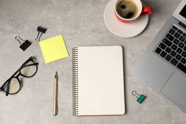 Not defteri, kalem, yapışkan not, cilt klipsleri, bardaklar, kahve ve dizüstü bilgisayar gri masada, düz yatıyordu.