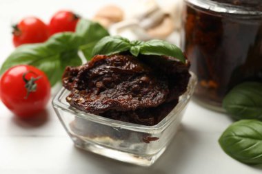 Lezzetli güneşte kurutulmuş domatesler, taze sebzeler ve fesleğenler beyaz masada, yakın plan.