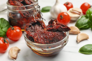 Lezzetli güneşte kurutulmuş domatesler, taze sebzeler, fesleğen ve sarımsak beyaz masada, yakın plan.