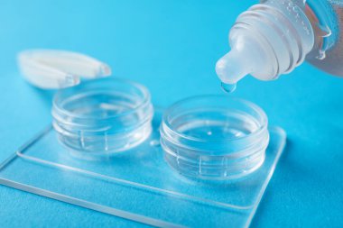 Açık mavi arkaplanda kontak lensleri olan çözelti dosyaya damlıyor, yakın plan