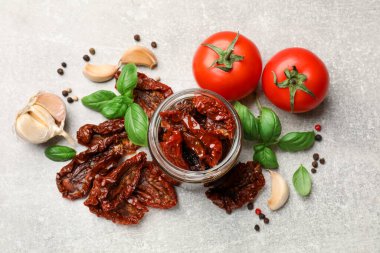 Lezzetli güneşte kurutulmuş domatesler, taze sebzeler ve baharatlar gri masada, düz yerde.