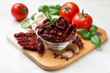 Lezzetli güneşte kurutulmuş domatesler, taze sebzeler ve baharatlar beyaz mermer masada, yakın plan.