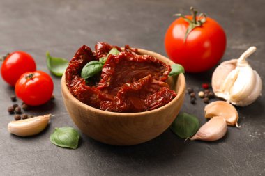 Lezzetli güneşte kurutulmuş domatesler ve taze sebzeler siyah masada, yakın plan.