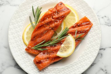 Deniz ürünleri. Beyaz mermer masada biberiye ve limonla servis edilen lezzetli ızgara somon.