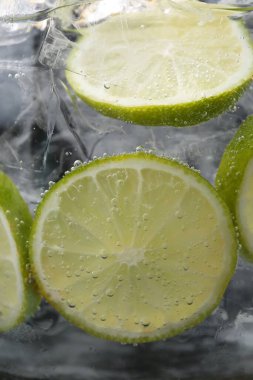 Koyu arkaplanda limon dilimleri ve buzla soda tazeleniyor. Yakın plan.