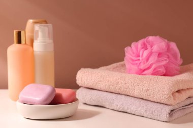 Açık kahverengi duvarın yanındaki beyaz masada farklı banyo ürünleri var.