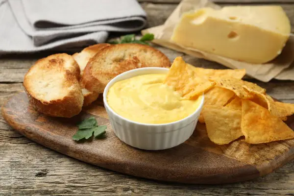 Lezzetli peynir sosu kaseye, nacho cipsi ve ekmek kırıntıları ahşap masaya, yakın plan.