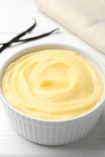Вкусный ванильный пудинг и стручки на белом деревянном столе, крупным планом