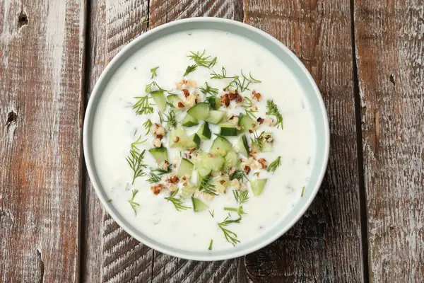 Ahşap masada dereotlu ve fındıklı lezzetli salatalık çorbası.