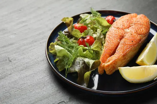 Deniz ürünleri. Siyah masada salata ve limonla servis edilen lezzetli somon bifteği, yakın plan. Metin için boşluk