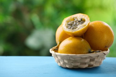 Açık mavi ahşap masada hasır sepetteki olgun çarkıfelek meyveleri, yakın plan. Metin için boşluk