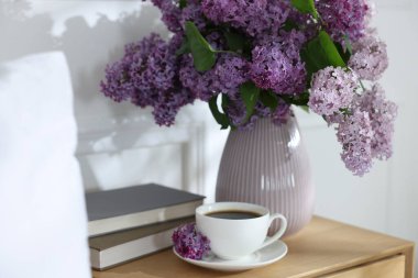 Komodinin üzerinde güzel leylak çiçekleri, kahve ve kitaplar.