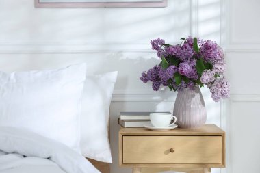Komodinin üzerinde güzel leylak çiçekleri, kahve ve kitaplar.