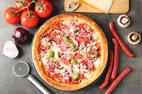 Tütsülenmiş sosisli lezzetli pizza, malzemeler ve gri desenli masa üzerinde makas, düz uzanma.
