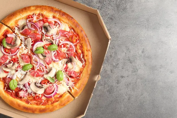Tütsülenmiş sosis ve karton kutuda mantarlı lezzetli pizza. Gri desenli masa, üst manzara. Metin için boşluk