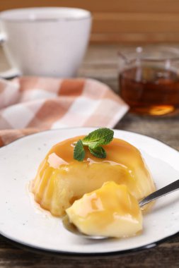 Karamel soslu lezzetli puding ve ahşap masada servis edilen nane, yakın plan.