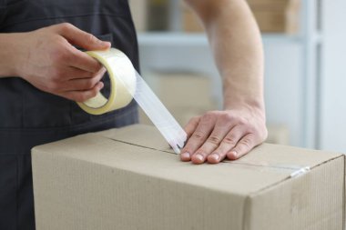Kapalı alanda yapıştırıcı bantlı karton kutu mühürleyen adam.