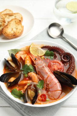 Beyaz ahşap masada servis edilen lezzetli deniz ürünleri çorbası, yakın plan.