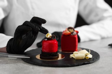 Mutfaktaki açık gri masada lezzetli bir tatlıyı dekore eden şekerci, yakın plan.