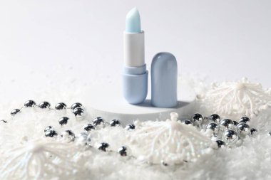 Nemlendirici dudak kremi ve yapay kar üzerindeki Noel süsü beyaz arka planda, yakın plan. Kış bakımı