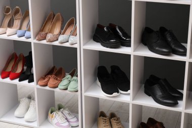 Ayakkabı deposu. Gri duvarın yanında farklı ayakkabıları olan raf ünitesi.