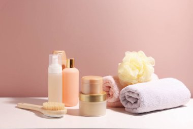 Açık kahverengi duvarın yanındaki beyaz masada farklı banyo ürünleri var.