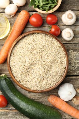 Tabaktaki çiğ kahverengi pirinç taze ürünlerin arasında, ahşap masada, düz yerde.