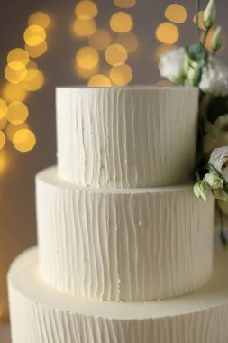 Gri arka planda çiçeklerle süslenmiş enfes düğün pastası. Bulanık ışıklar, yakın plan.