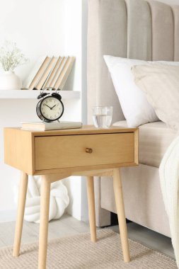 Alarmlı komodinli komodin, bir bardak su ve yatağın yanında kitap.