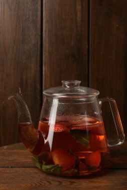 Çilekli Aromatik meyve çayı ve ahşap masada cam çaydanlık.