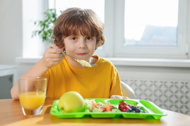 Okuldaki ahşap masada yemek yiyen şirin küçük çocuk.