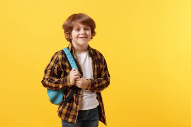 Turuncu arka planda sırt çantası olan tatlı bir okul çocuğu, mesaj için yer var.