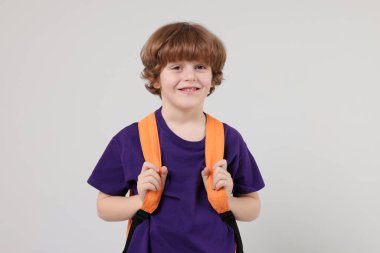Açık gri arka planda sırt çantası olan sevimli bir okul çocuğu.