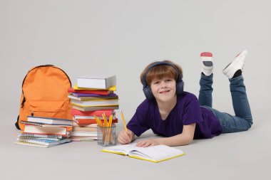 Sırt çantası ve defterine açık gri arkaplan çizen sevimli okul çocuğu.