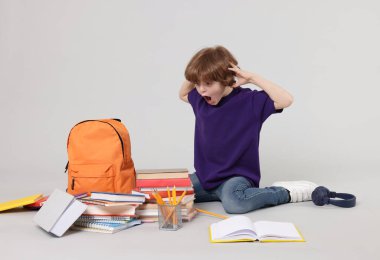 Sırt çantası, kitapları ve açık gri arka planda farklı kırtasiyeleri olan sevimli bir okul çocuğu.