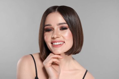 Açık gri arka planda muhteşem düz saçları olan güzel, genç bir kadının portresi.