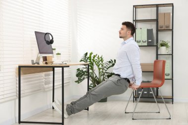 Ofiste sandalyeyle egzersiz yapan yakışıklı adam.