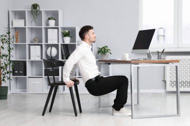 Ofiste sandalyeyle egzersiz yapan yakışıklı adam.