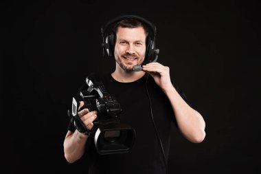 Profesyonel kameralı ve kulaklıklı bir adam siyah arka planda.