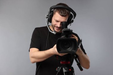 Profesyonel kameralı ve kulaklıklı bir adam gri arka planda.