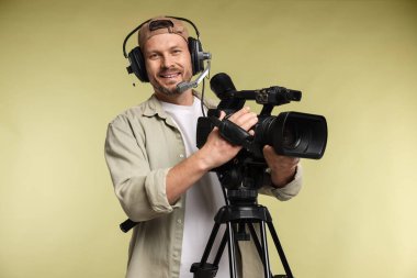 Profesyonel kamera ve soluk zeytinli arka planda kulaklığı olan bir adam.