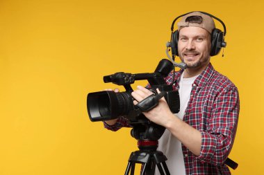 Profesyonel kamera ve turuncu arka planda kulaklığı olan bir adam.