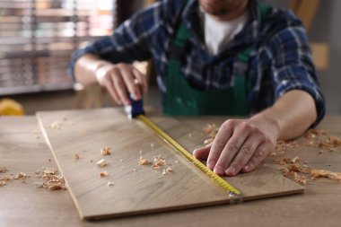 İçerideki ahşap masada bant ve kalemle tahta ölçen adam, yakın plan.