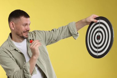 Hedef alınıyor. Sarı arka planda ok ve dart tahtası olan adam.